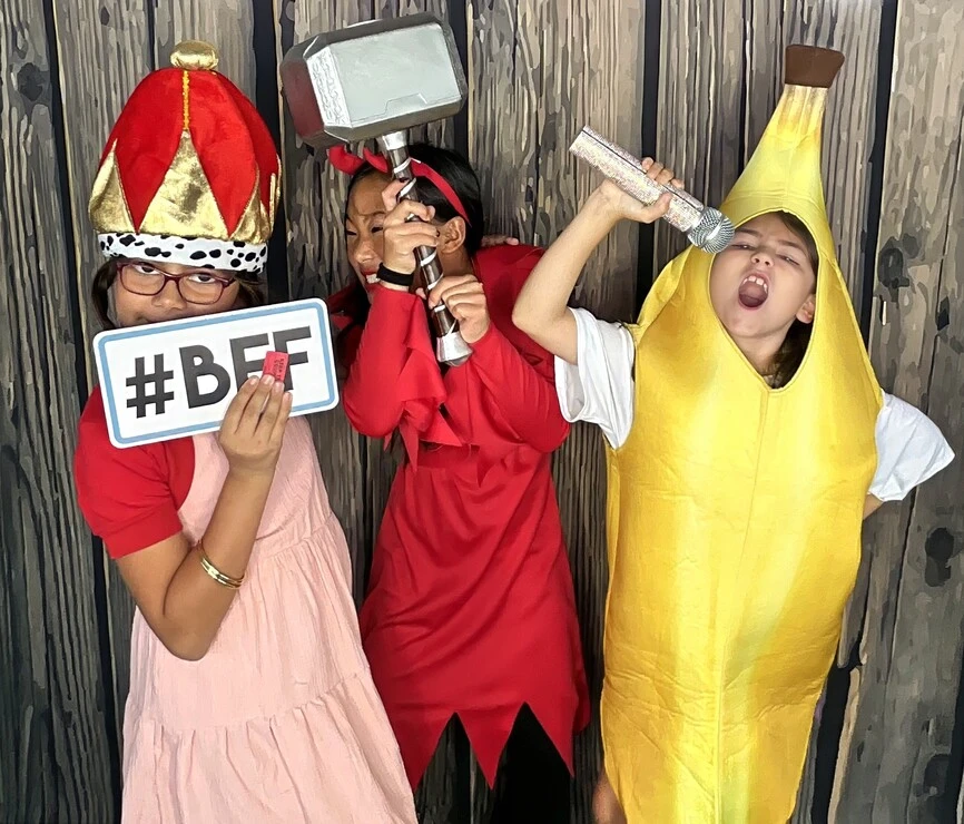 Children pose with playful photo booth props at a Halloween costume party.