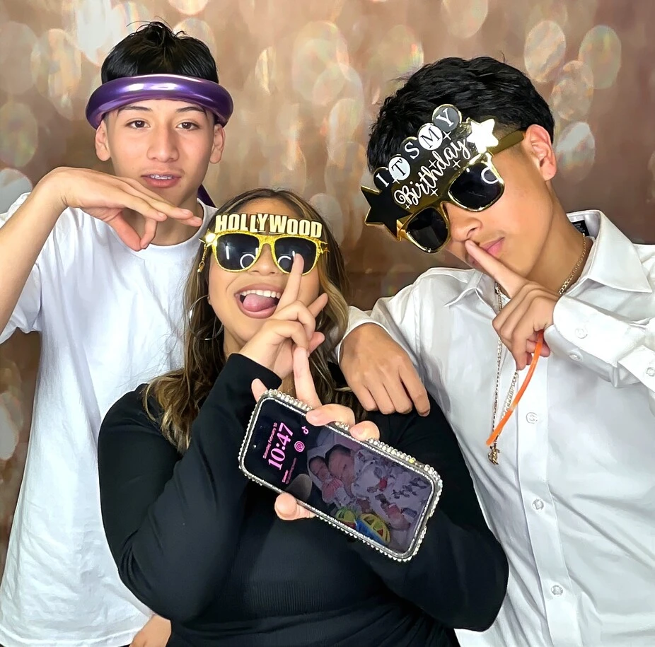 Friends pose with playful photo booth props at a Sweet 16 celebration.