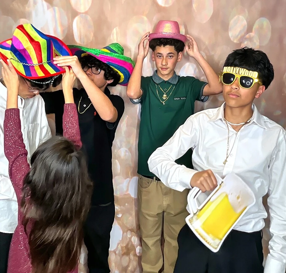Friends pose with playful photo booth props at a quinceañera celebration.