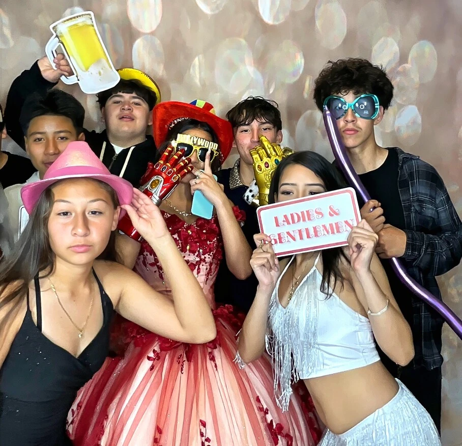 Friends pose with playful photo booth props at a quinceañera celebration.