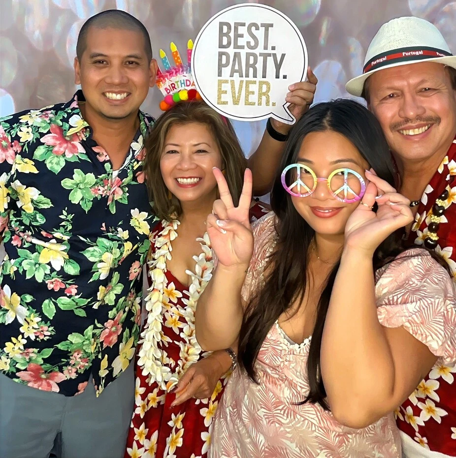 Guests pose with playful photo booth props at a tropical-themed party.
